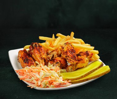 Bir tabak kızarmış tavuk kanadı patates kızartması ve salata.