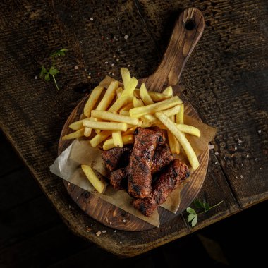 Izgara evi konsepti. Kızarmış, kızarmış sosis ve patates kızartması eski ahşap kesim tahtasının üstünde..