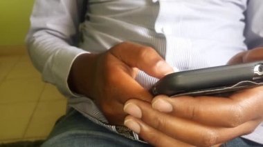 Telefonunu tamir etmekle meşgul genç bir adama yaklaş. Çizgili resmi bir gömlek giyiyor. İş konsepti. Daktilo, mesaj, araştırma. Kopyalama. - Evde. Cep telefonu görüntülerini kullanarak.