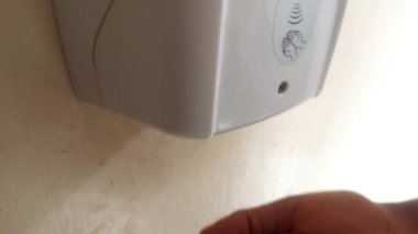 Duvar görüntülerinde otomatik dezenfektan kullanan kahverengi bir el. Adam elini şeker kutusunun altına koyuyor, elini dezenfektan sıvısıyla ıslatırken yeşil ışık yanıyor. Elini hareket ettiriyor ve ateş alıyor. Video klibi.