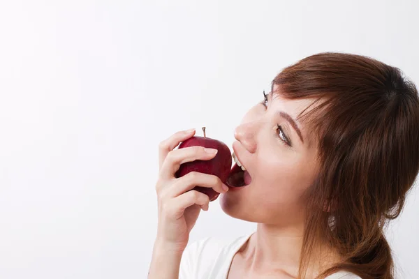 Здорова азіатка, дивлячись вгору, кусає, їсть червоне яблуко — стокове фото