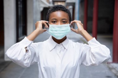 Açık alanda yüz maskesi takan genç Afrikalı bir kadın.