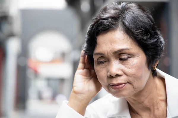 Asian senior woman listening to something; portrait of sad old asian female elderly with hearing ear, concept of rumor, gossip, hearing loss, hard of hearing, fake news, bad news or information