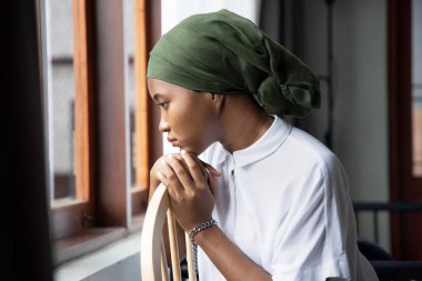 Üzgün Afrikalı genç kadın kanser hastasının portresi hastalıkla mücadele ediyor, kemoterapi, kanser farkındalığı gibi ciddi saç dökülmesi yan etkilerinden sonra başörtüsü takıyor.