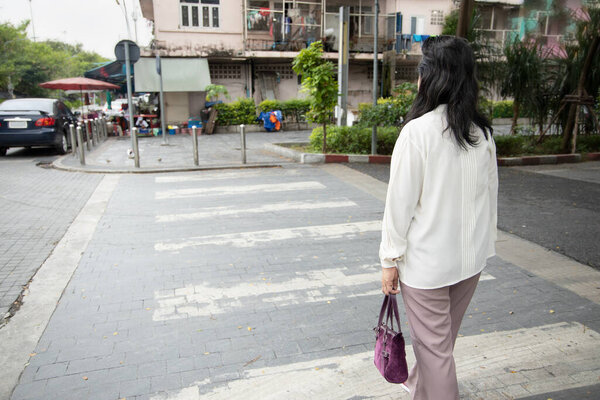 middle aged asian woman crossing the road on zebra crossing, traffic safety concept