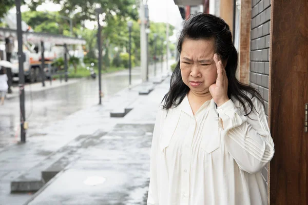 stressed, depressed asian senior woman suffering from headache