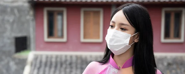 屋外の公共スペースで顔マスクを適切に身に着けている若いアジアベトナム人女性のバナー — ストック写真