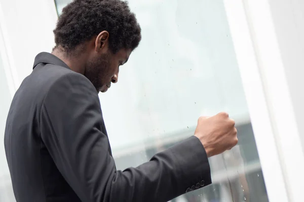 Angry upset African black businessman, portrait of failed unhappy black business man punching glass window, concept of work problem, office stress syndrome, economic recession, layoff, unemployment