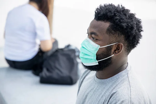 Asymptometic black African man wearing hygienic face mask and stay away from other people as prevention measure to stop spreading the pandemic COVID-19 disease while waiting for vaccine