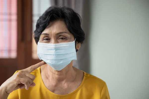 old senior woman pointing at face mask, concept of mouth and nose covering face mask wearing, fine dust pollution, air pollution, COVID-19 contagious disease preventive medicine