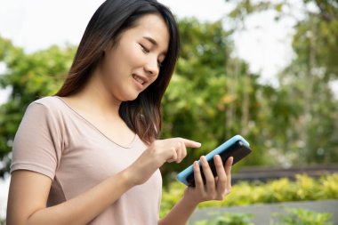 Mutlu Asyalı kadın kablosuz akıllı telefon şarjı kullanıyor, taşınabilir kablosuz indüksiyon güç bankası pili cihazı.