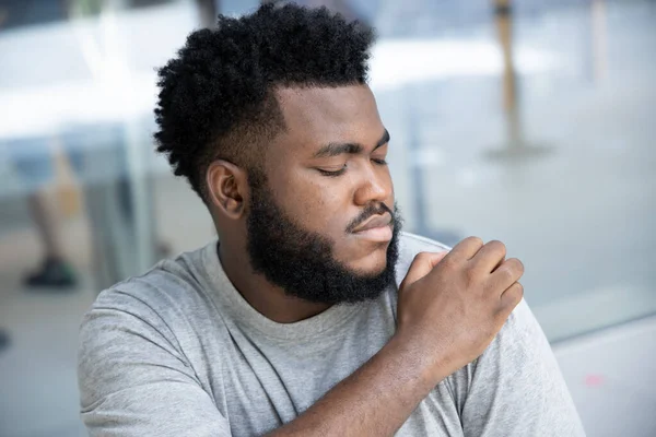 Man scratching suffering from itching shoulder skin; sick African man scratching his skin with allergy, rash, ringworm, tinea problem; skin care, dermatology concept; adult black African man model