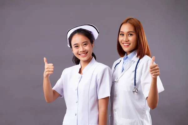 Happy professional female doctor and nurse, medical team, health care worker pointing thumb up on isolated background