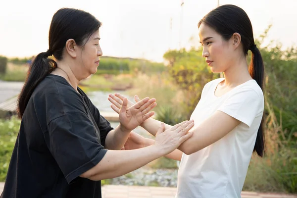 Asian old woman working out with practicing taichi push hand with young woman, traditional fitness style