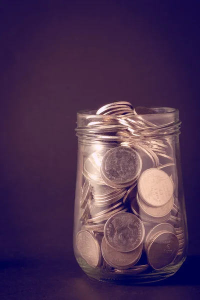 Coins spilling out of a glass bottle with filter effect retro vi — Stock Photo, Image