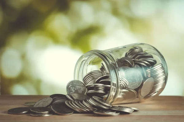 Coins spilling out of a glass bottle with filter effect retro vi — Stock Photo, Image