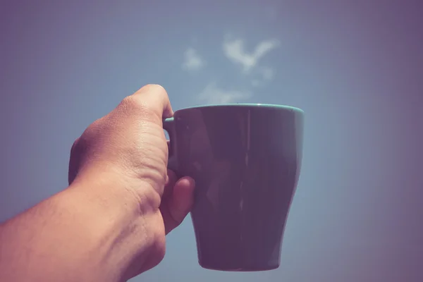 Man håller kaffekoppen i handen framför blå himmel — Stockfoto