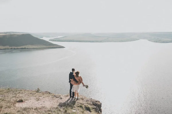 De bruidegom en bruid staan op een klif voor een groot stuwmeer in de verte zijn eilanden — Stockfoto