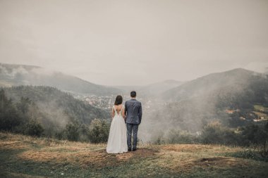  Gelin, sırtında damatla birlikte siste, dağlarda duruyor.