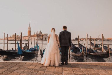 Venedik 'te bir düğün çifti rıhtımda duruyor. Tekneler suda yüzer