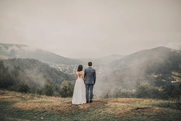 Gelin, sırtında damatla birlikte siste, dağlarda duruyor. — Stok fotoğraf