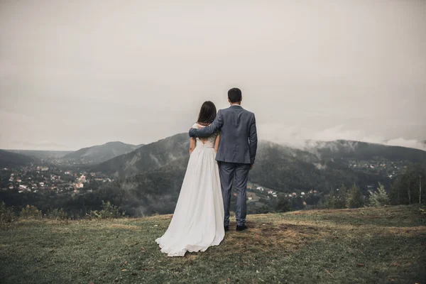 Bruden står med ryggen med brudgummen vid bergen i dimman — Stockfoto