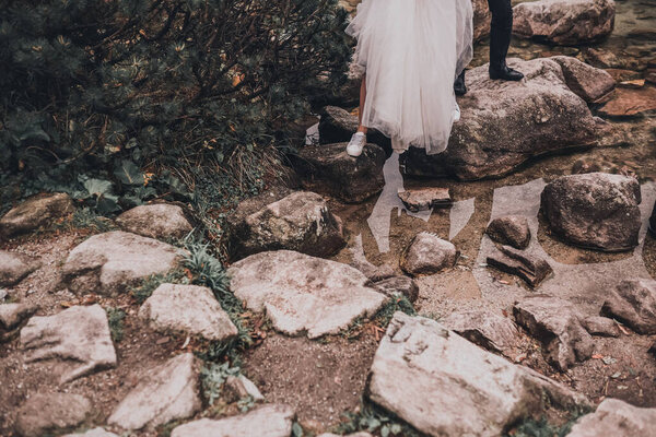 A legs of couple newlyweds In wedding clothes. a transparent water and gray stones. bride in a white long dress and a slim man groom