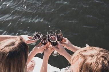 Bekarlığa veda partisinde giyinmiş kızlar bardaktan kırmızı şarap içiyor.