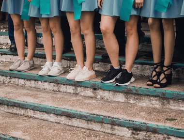 Zayıf kızlar, mavi etekli, farklı ayakkabılı bacaklar, birlikte basamaklarda dururlar.