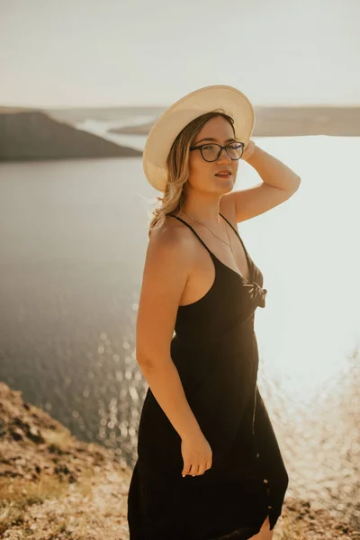 Mulher com chapéu e óculos fica em um penhasco sobre o mar — Fotografia de Stock