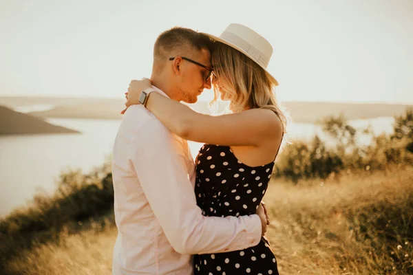En man med en kvinna i hatt kram och kyss i det höga gräset på ängen — Stockfoto