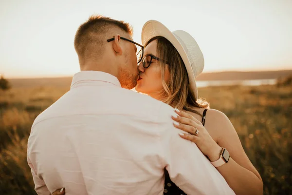 Um homem com uma mulher de chapéu abraçando e beijando na grama alta no prado — Fotografia de Stock