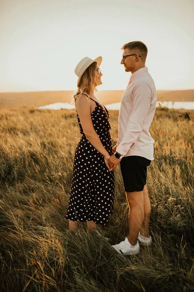 A man with a woman in a hat hug and kiss in the tall grass in the meadow — Stock Photo, Image