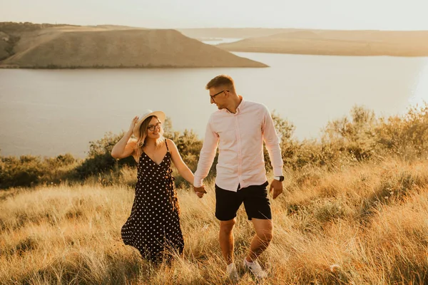 Man och kvinna promenader på ängen vid solnedgången på sommaren nära sjön — Stockfoto