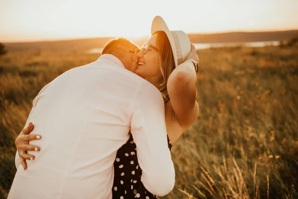 Um homem com uma mulher de chapéu abraçando e beijando na grama alta no prado — Fotografia de Stock