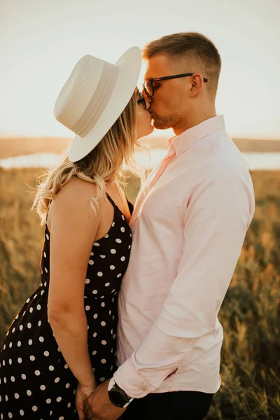 Een man met een vrouw in een hoed knuffelen en kussen in het hoge gras in het weiland — Stockfoto