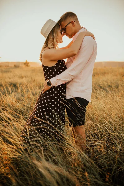 Um homem com uma mulher de chapéu abraçando e beijando na grama alta no prado — Fotografia de Stock