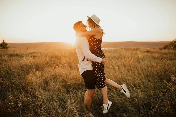 Un hombre con una mujer en un sombrero abrazo y beso en la hierba alta en el prado —  Fotos de Stock