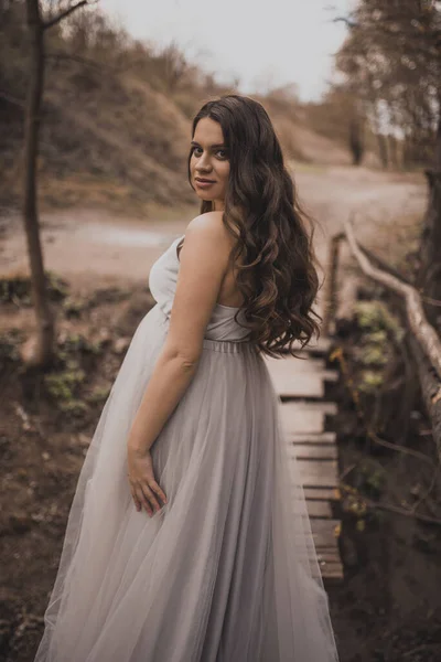 Mulher grávida perto de montanhas caminha ao longo de uma ponte de madeira — Fotografia de Stock