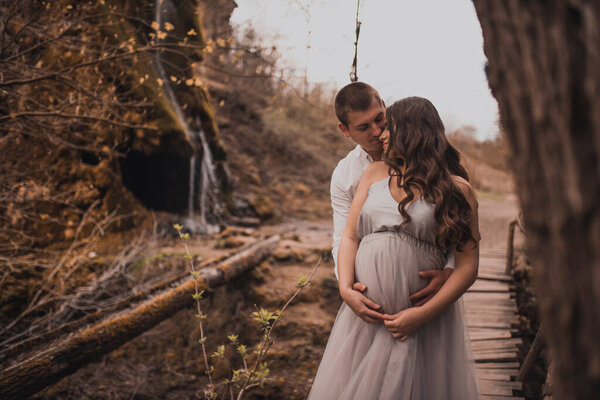 Family couple a man with a pregnant woman with a big belly in nature on the background of a waterfall. wooden bridge
