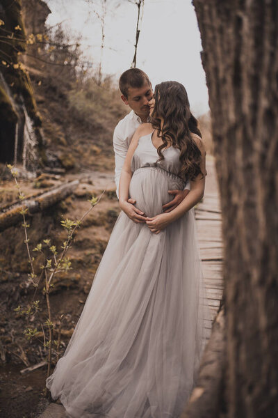 Family couple a man with a pregnant woman with a big belly in nature on the background of a waterfall. wooden bridge