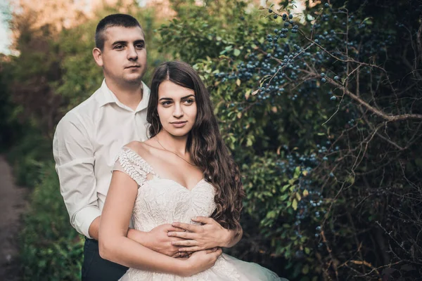 Mariée et marié en robe de mariée sur fond de buisson vert avec des baies bleues floues. — Photo