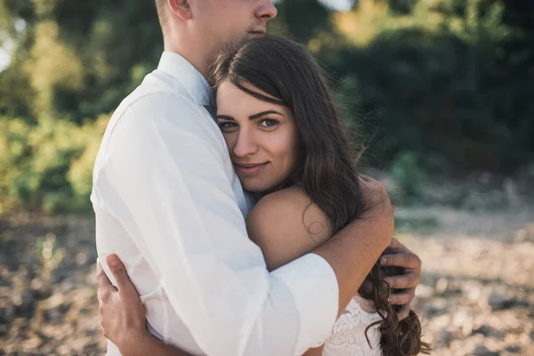 Brudgum och brud står i omfamning på stenig strand nära floden på sommaren — Stockfoto