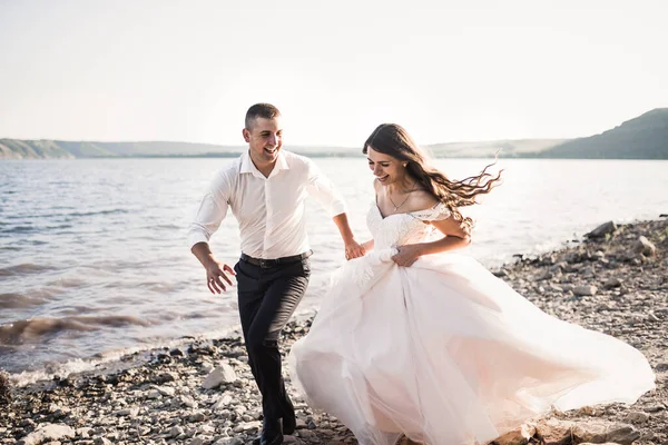 bride and groom laughing run together against rays of setting sun in summer