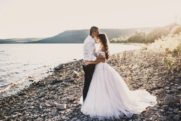 Novio y novia de pie en abrazo en la orilla rocosa cerca del río en verano —  Fotos de Stock