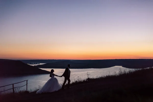 Siluetas de novia y novio en la noche contra el lago y las islas —  Fotos de Stock