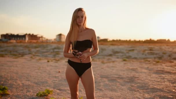 Mujer en bikini negro traje de baño con pelo largo se levanta en la playa — Vídeos de Stock