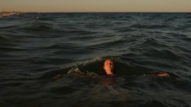 Tersine çevrilebilir video. Kız sudan yükselir. Genç seksi kadın gün batımında bikini mayosuyla denizde yüzer.