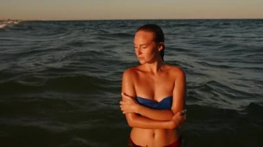 Kameraya bakan kadın gün batımında bikinili mayo giymiş büyük dalgalar üzerinde suya düşer.