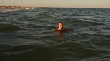 Genç seksi kadın gün batımında bikini mayosuyla denizde yüzer.